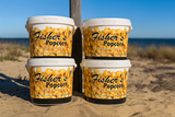 Four large tubs of Fisher’s Popcorn stacked on sandy ground near a beach, with blue sky and ocean visible in the background.