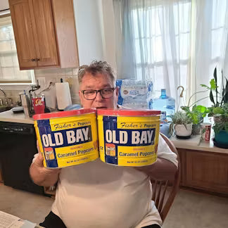 Person holding two Old Bay seasoning containers in a kitchen.