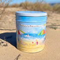 Fisher’s Popcorn 3.5 Gallon Beach Tin features a colorful beach scene with umbrellas, a child, and the ocean on sandy dunes under a blue sky—making it the perfect popcorn gift.