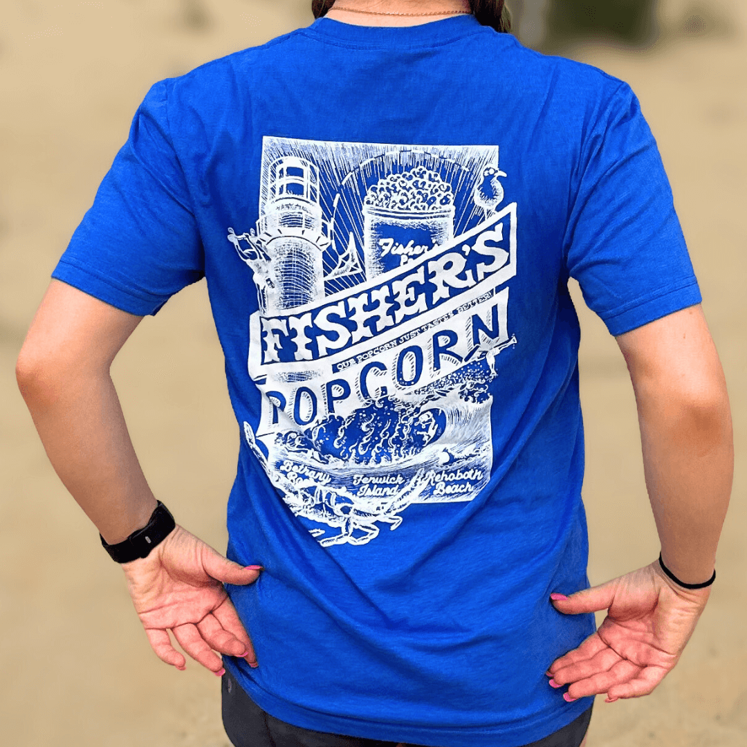 Someone wears the Fisher's Popcorn Fisher's T-Shirt in bright blue, featuring a white lighthouse, popcorn bucket, waves, and text: “Fisher’s Popcorn, Fenwick Island, Boardwalk, Beach”—a perfect beach tee for popcorn fans.