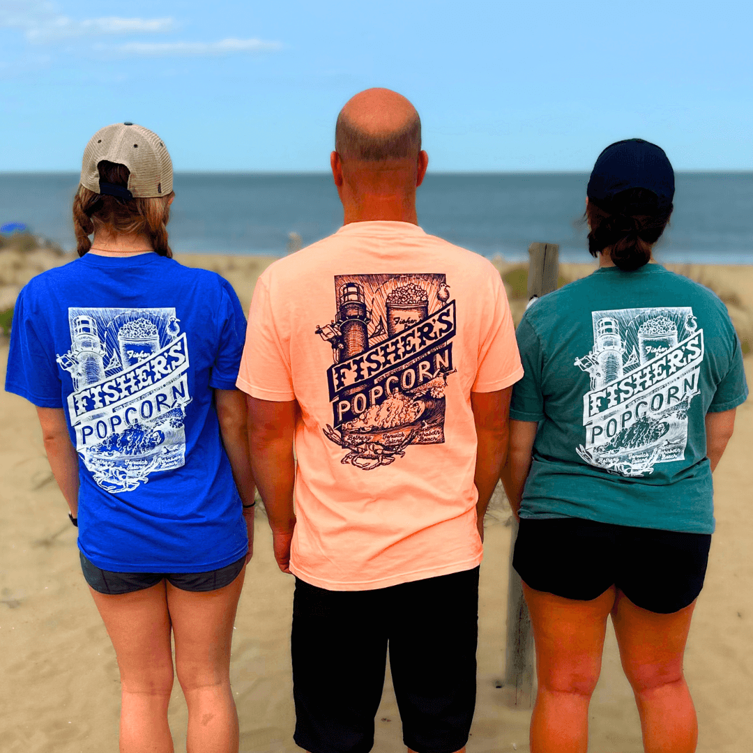 Three people stand on a sandy beach facing the ocean, each sporting a Fisher’s T-Shirt from Fisher’s Popcorn—a perfect day by the sea to show off your favorite beach shirt from this iconic popcorn brand.
