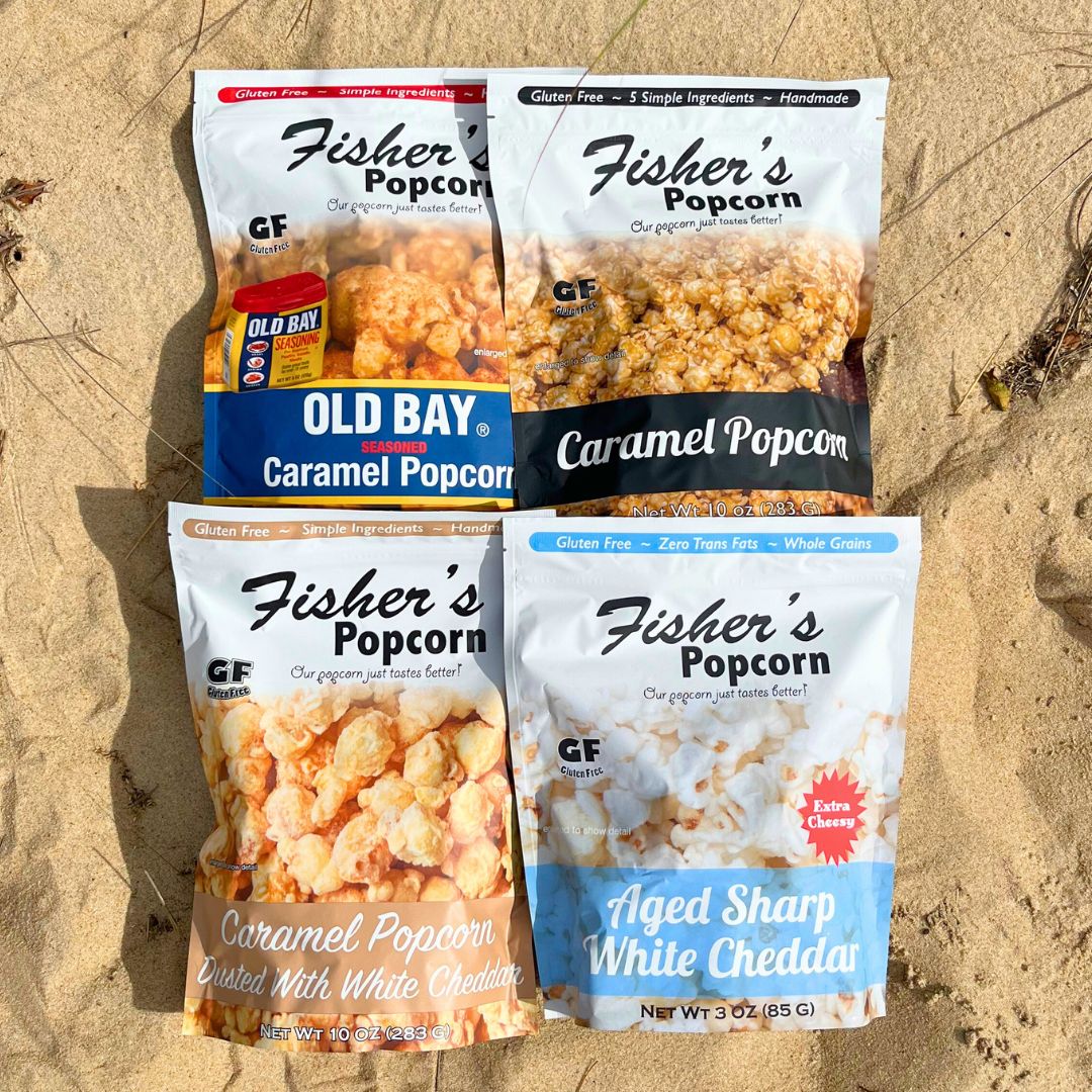 Four Fisher's Popcorn Large Popcorn Bags—Old Bay Caramel, Caramel, Caramel Dusted with White Cheddar, and Aged Sharp White Cheddar—offer bold flavors in resealable bags with vibrant packaging.