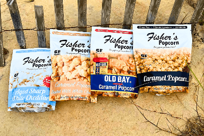 Four packages of Fisher's Popcorn on a sandy background