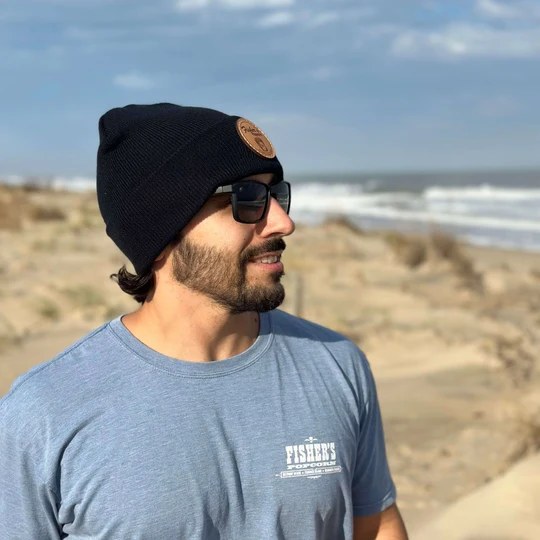 Man in a black Fisher's beanie and a blue Fisher's tee on the dunes